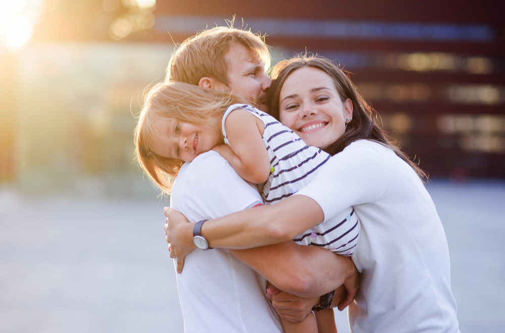 Father and mother hugging little girl and smiling together wearing white clothes