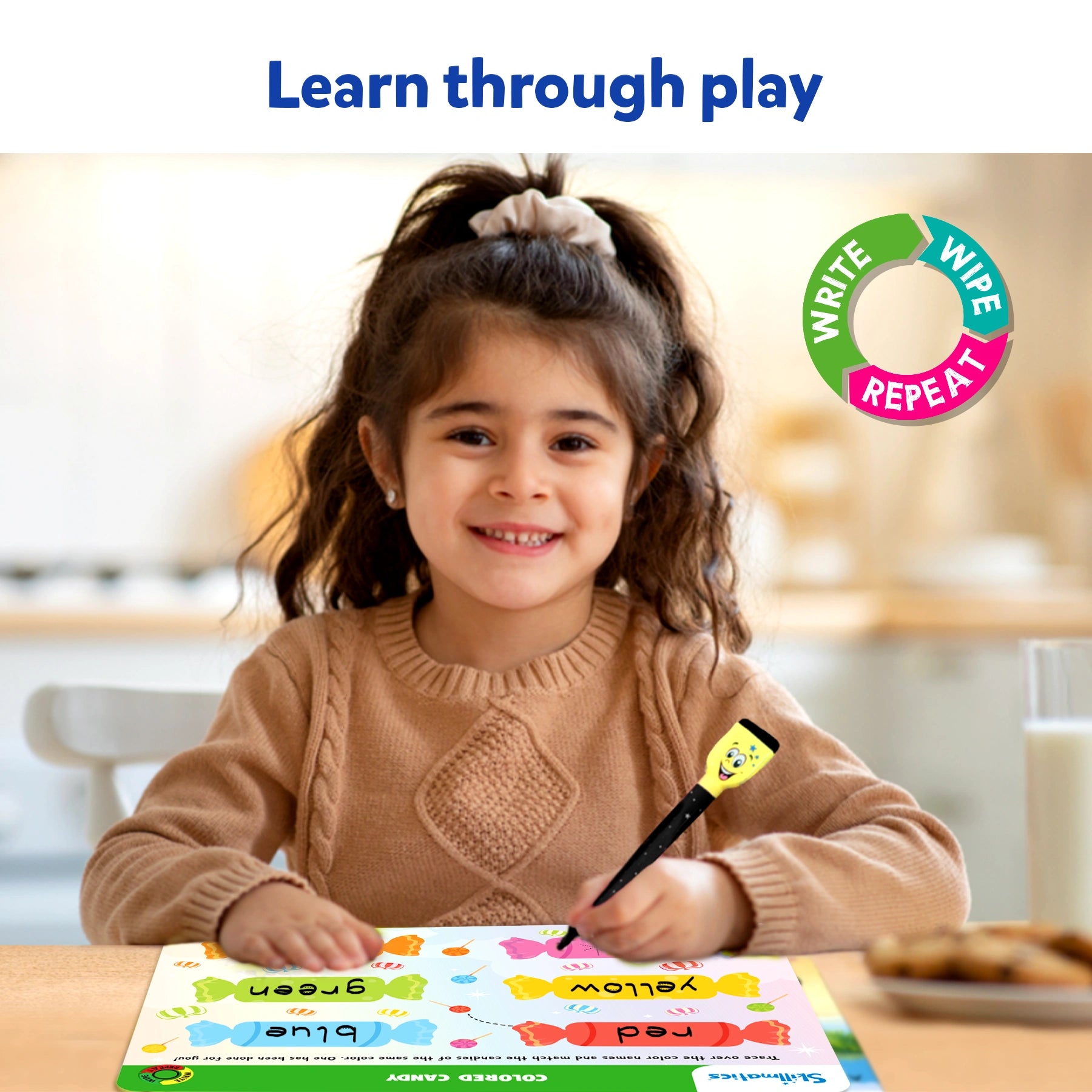 Young girl smiling while using a Skillmatics Preschool Champion reusable activity mat at a table. She holds the yellow dry-erase marker while completing a colorful activity sheet that teaches colors and words. Text overlay reads “Learn through play.”