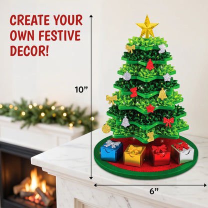 Poke-In Art Christmas Tree displayed on a white mantel beside a lit fireplace, with arrows showing its 10-inch height and 6-inch width. The green layered tree has glitter ornaments, a golden star, four mini gift boxes and a red circular base. 