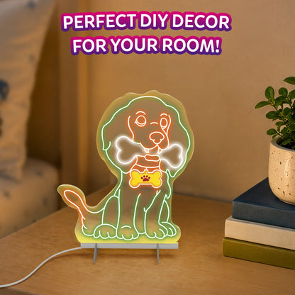 Glowing dog-shaped Light-Up Sketcher displayed on a wooden tabletop in a room setting, with a white power cable extending from its base. The neon-style dog has a bone-shaped tag and bright green and orange outlines, beside stacked books and a potted plant.
