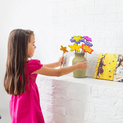 Young girl in a pink dress arranging poke-in fabric flowers into a vase on a white shelf. The colorful flowers are made from the kit’s foam shapes and fabric squares.