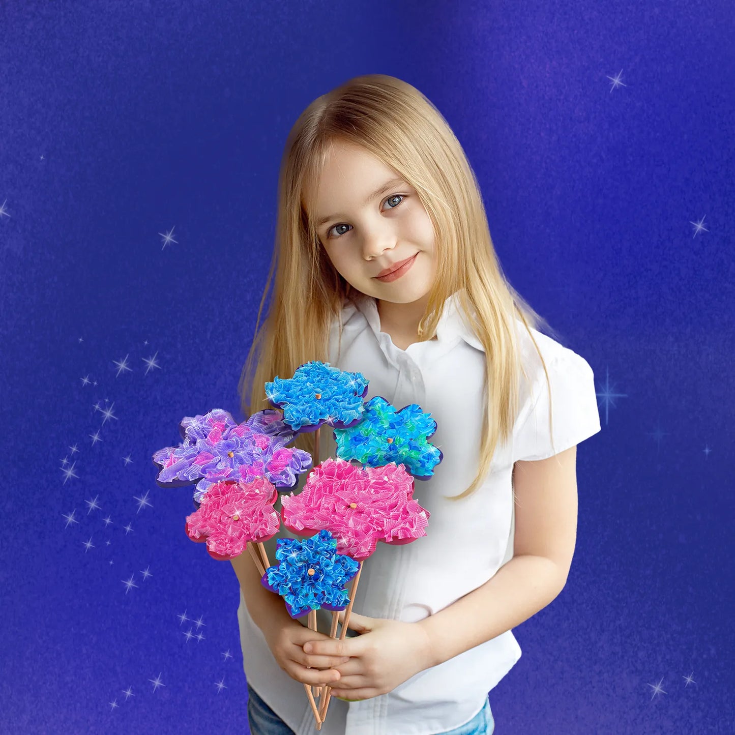 Smiling blonde girl holding a handmade bouquet of poke-in fabric flowers in pink, purple, and blue, standing against a purple starry background.