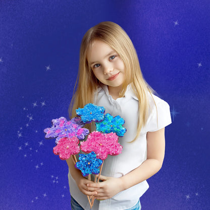 Smiling blonde girl holding a handmade bouquet of poke-in fabric flowers in pink, purple, and blue, standing against a purple starry background.